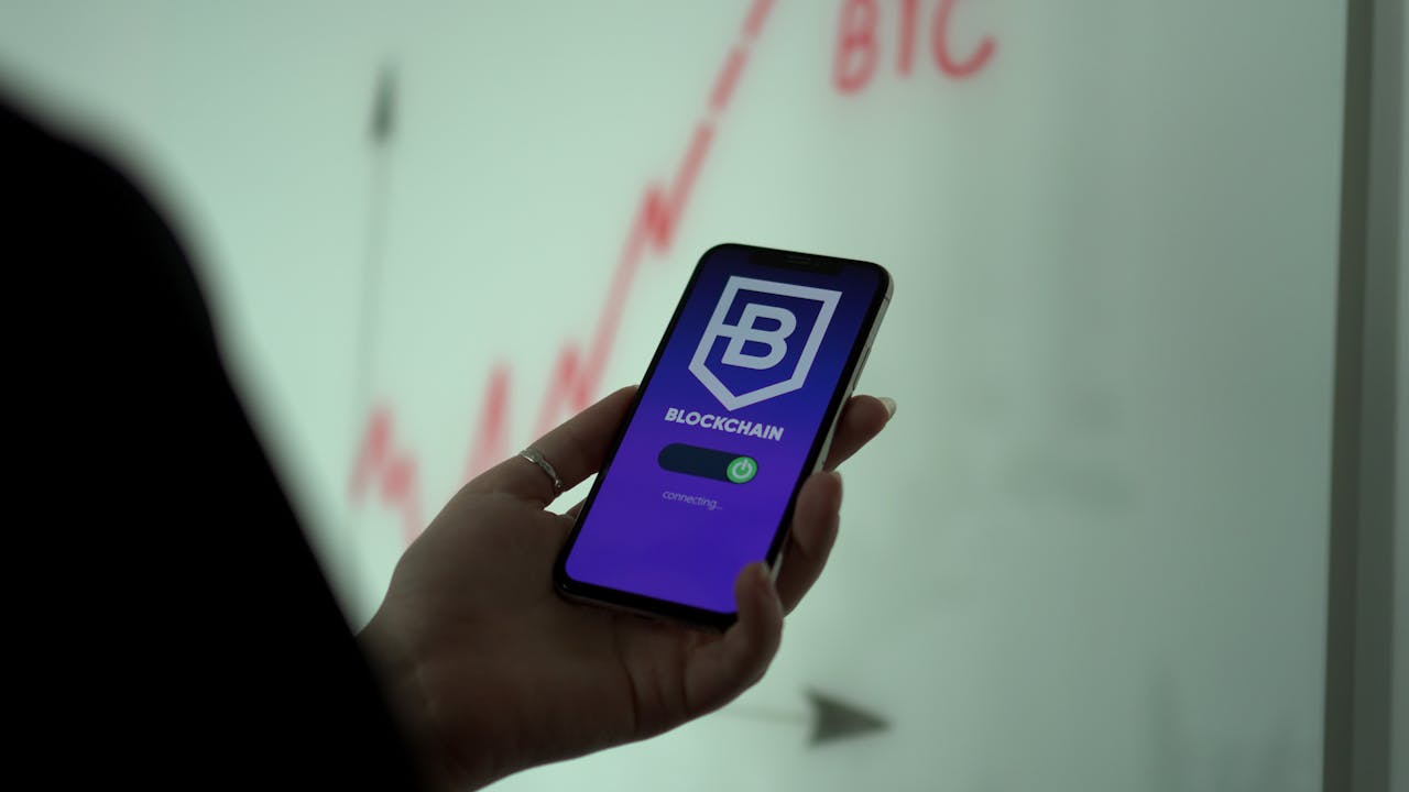 Mastering the First Impression: Your intriguing post title goes here A close-up of a hand holding a smartphone displaying a blockchain app with a stock graph in the background.